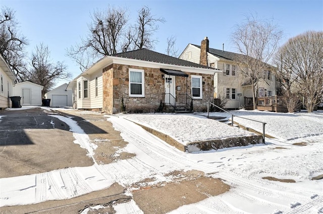 view of front of house with driveway, stone siding, a detached garage, a chimney, and an outdoor structure