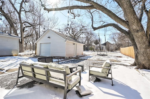 snow covered patio featuring an outbuilding, a detached garage, and fence