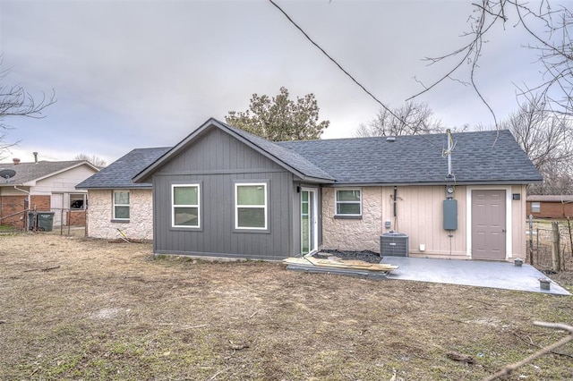 rear view of property with stone siding, roof with shingles, a patio area, and fence