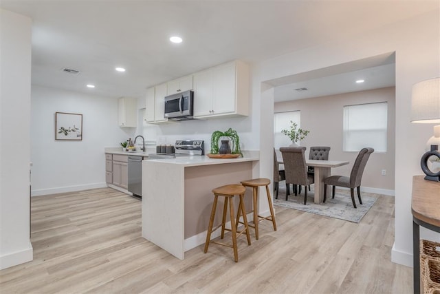 kitchen featuring a breakfast bar, stainless steel appliances, light countertops, white cabinets, and a peninsula