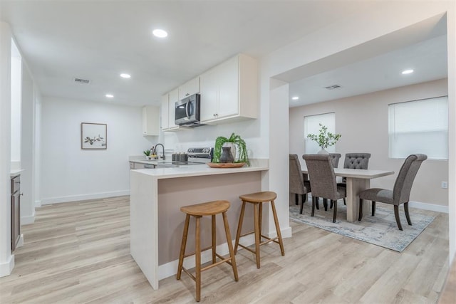 kitchen featuring a breakfast bar area, stainless steel appliances, white cabinets, light countertops, and light wood-type flooring