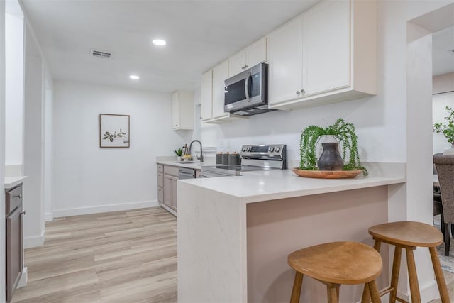 kitchen with light countertops, visible vents, appliances with stainless steel finishes, white cabinets, and a kitchen bar