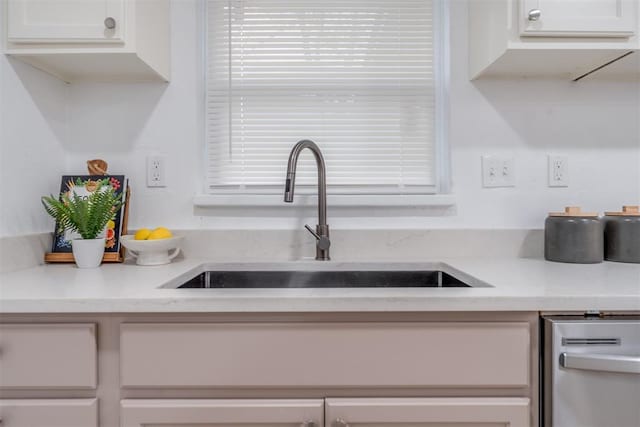 kitchen with stainless steel dishwasher, a sink, and white cabinetry