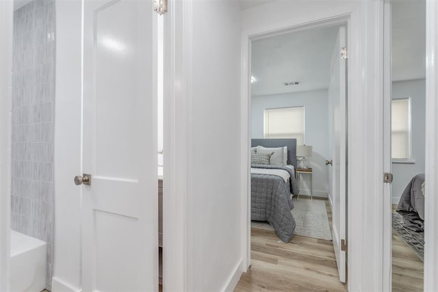 hall with baseboards, visible vents, and light wood-style floors