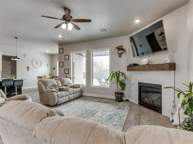 living area featuring visible vents, baseboards, a glass covered fireplace, ceiling fan, and wood finished floors