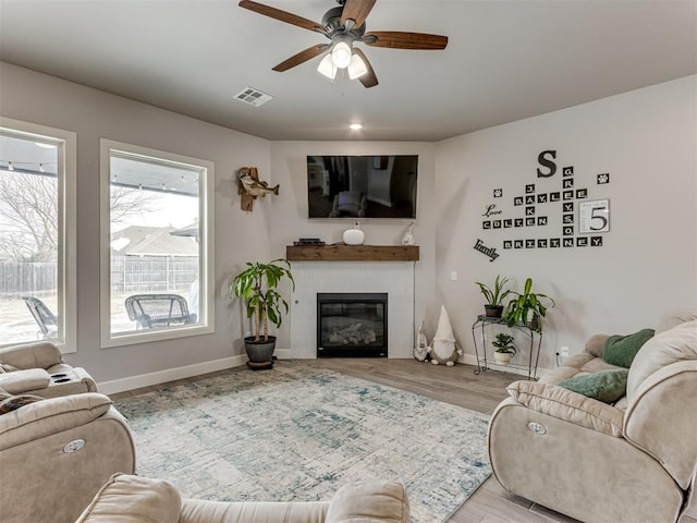 living room with ceiling fan, wood finished floors, visible vents, baseboards, and a glass covered fireplace