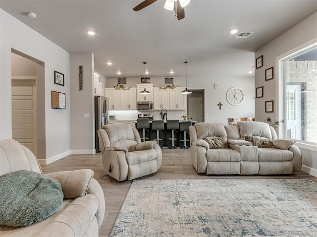 living area with light wood-type flooring, ceiling fan, visible vents, and recessed lighting