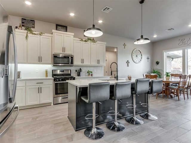 kitchen with tasteful backsplash, light countertops, visible vents, appliances with stainless steel finishes, and an island with sink