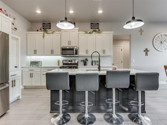 kitchen featuring a breakfast bar, light countertops, appliances with stainless steel finishes, tasteful backsplash, and an island with sink