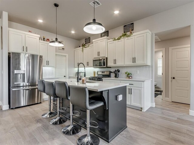 kitchen featuring a breakfast bar area, stainless steel appliances, visible vents, light countertops, and backsplash