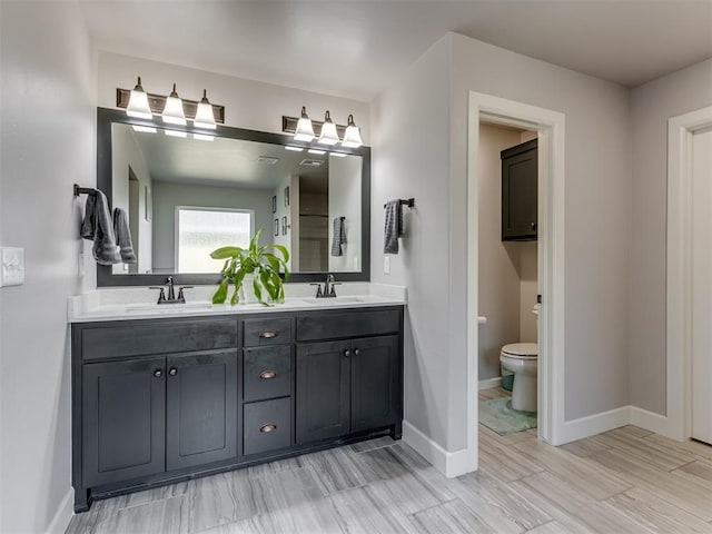 full bath featuring baseboards, a sink, toilet, and double vanity