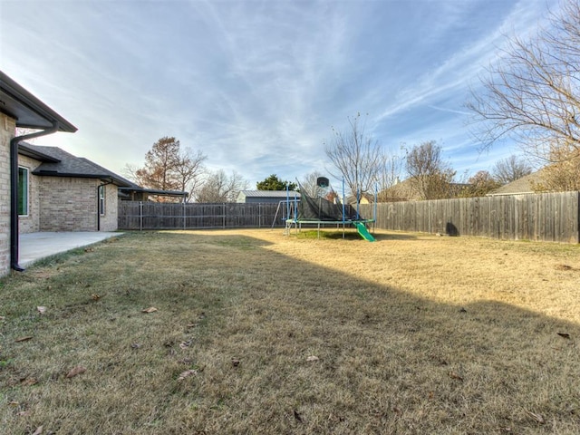 view of yard featuring a trampoline, a fenced backyard, and a patio