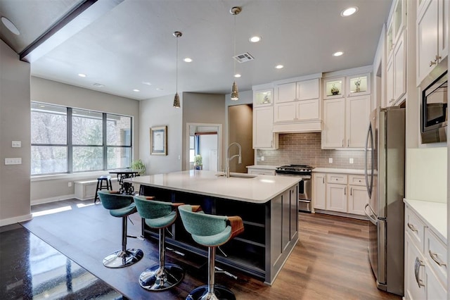 kitchen with visible vents, an island with sink, glass insert cabinets, stainless steel appliances, and light countertops