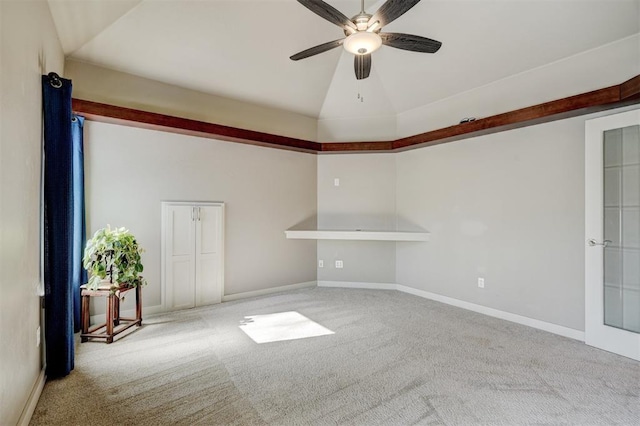 empty room with lofted ceiling, ceiling fan, baseboards, and light colored carpet