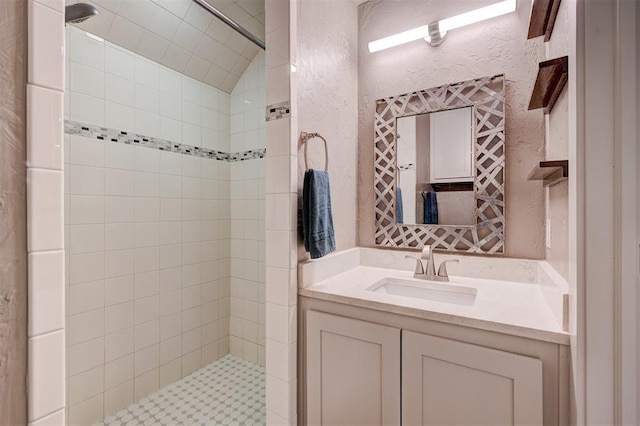 full bathroom featuring a textured wall, a tile shower, and vanity