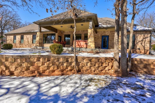 snow covered house featuring brick siding and ceiling fan