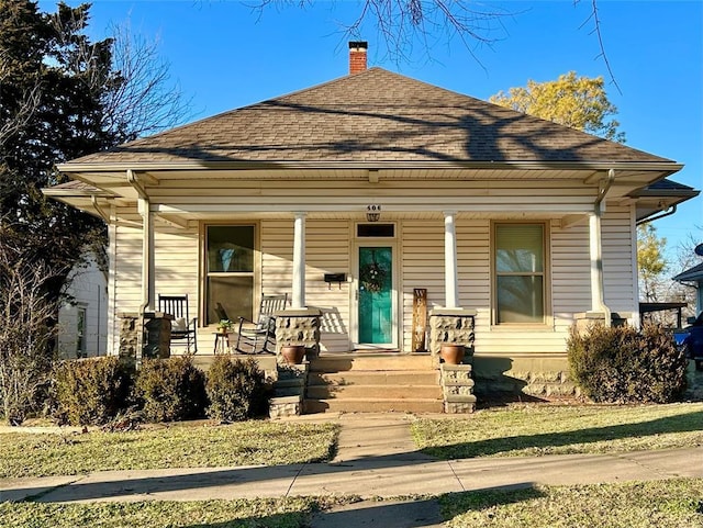 bungalow featuring covered porch, roof with shingles, and a chimney