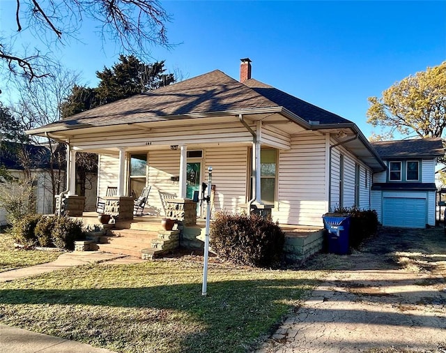 bungalow-style house with covered porch, roof with shingles, a front lawn, and a chimney