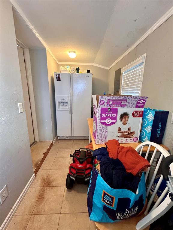 kitchen featuring light tile patterned floors, white refrigerator with ice dispenser, baseboards, and crown molding