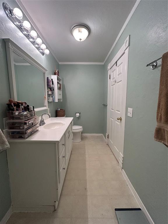 bathroom with baseboards, vanity, toilet, and crown molding