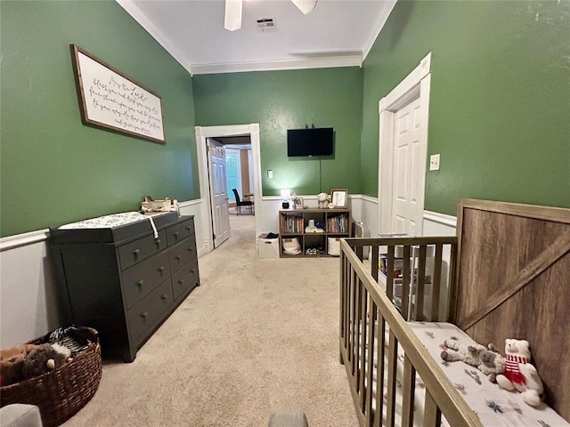 bedroom with a wainscoted wall, crown molding, visible vents, light carpet, and a crib