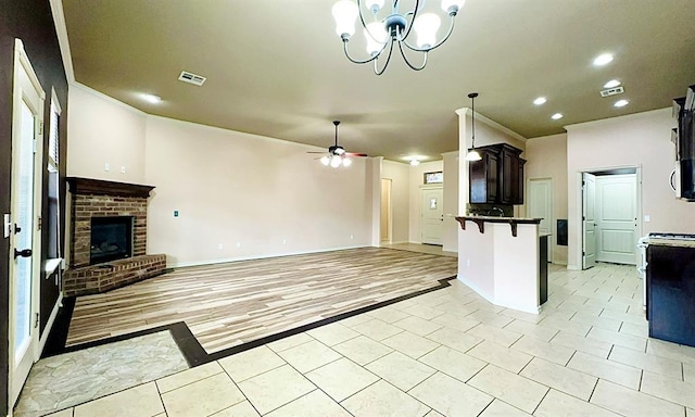 kitchen with ceiling fan with notable chandelier, a fireplace, a kitchen breakfast bar, open floor plan, and dark countertops