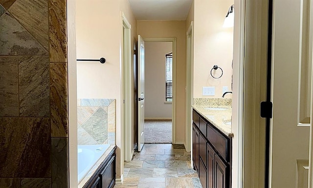 bathroom with a washtub, double vanity, stone finish flooring, a sink, and baseboards