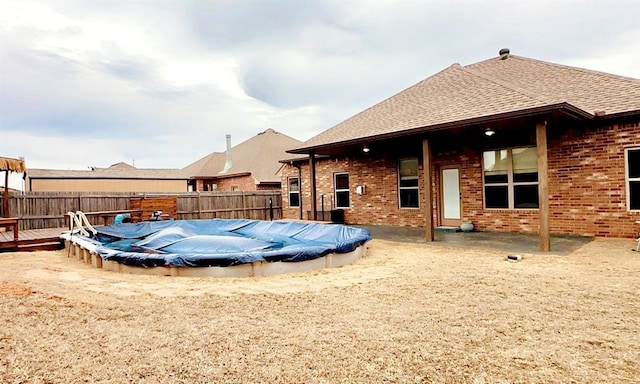 rear view of property featuring roof with shingles, fence, a fenced in pool, and brick siding