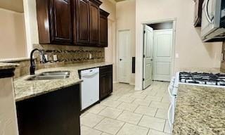 kitchen featuring dark brown cabinetry, dishwasher, light stone counters, stainless steel microwave, and a sink