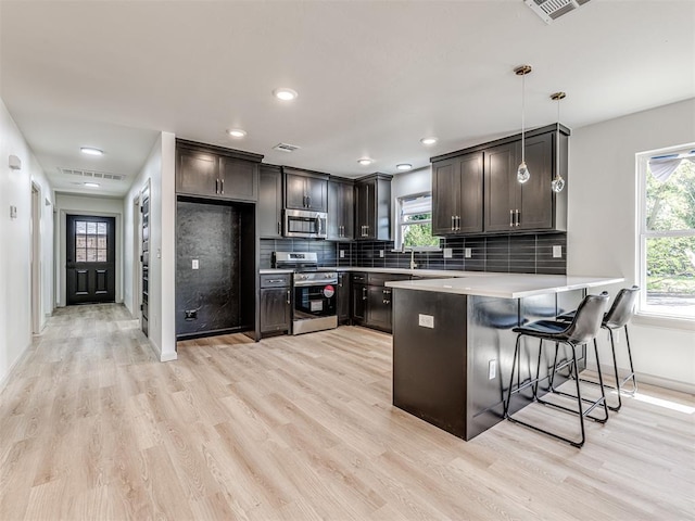 kitchen featuring light countertops, a peninsula, light wood finished floors, stainless steel appliances, and decorative backsplash