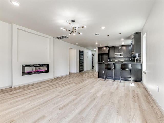 kitchen with stainless steel microwave, light wood finished floors, visible vents, and backsplash