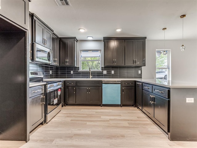 kitchen featuring a wealth of natural light, light wood finished floors, a peninsula, and stainless steel appliances