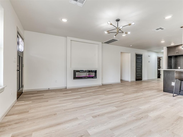 unfurnished living room featuring visible vents, heating unit, a chandelier, and a glass covered fireplace