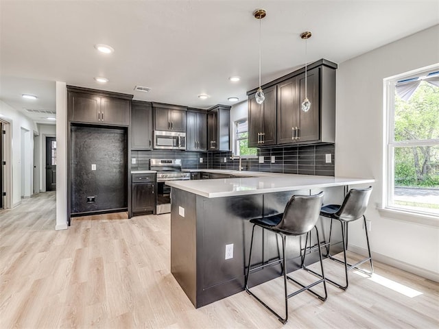 kitchen with a wealth of natural light, a peninsula, visible vents, stainless steel appliances, and light wood finished floors