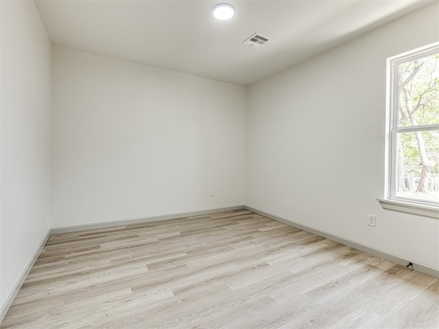 empty room featuring light wood finished floors, baseboards, and visible vents
