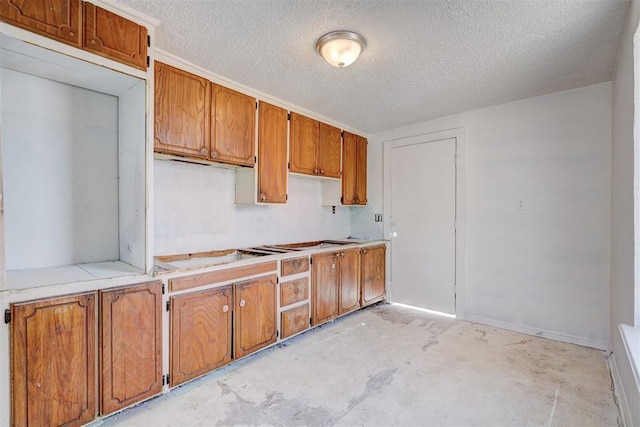 kitchen with a textured ceiling, light countertops, brown cabinetry, and unfinished concrete flooring