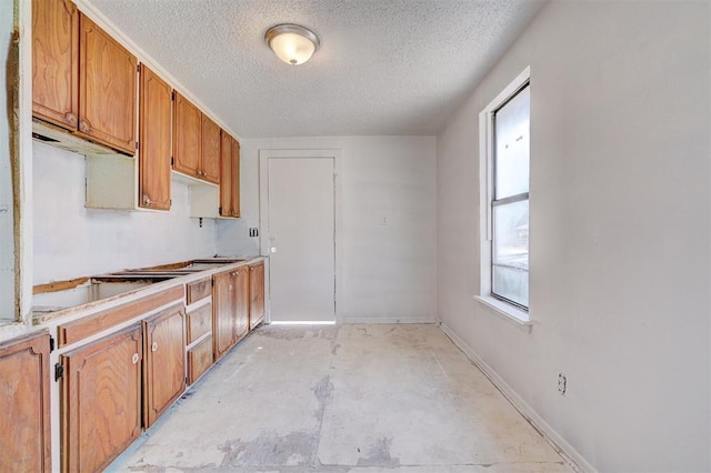 kitchen featuring baseboards, brown cabinetry, unfinished concrete floors, light countertops, and a textured ceiling