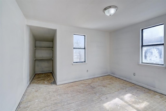 unfurnished bedroom with a walk in closet, a closet, multiple windows, and baseboards