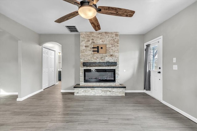 unfurnished living room with baseboards, visible vents, arched walkways, wood finished floors, and a fireplace