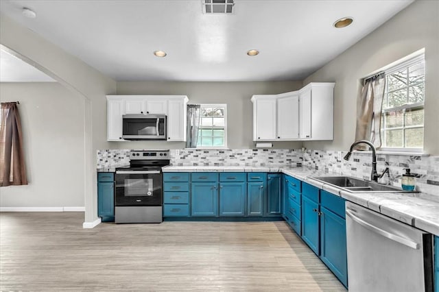 kitchen with a sink, white cabinetry, light countertops, appliances with stainless steel finishes, and blue cabinetry