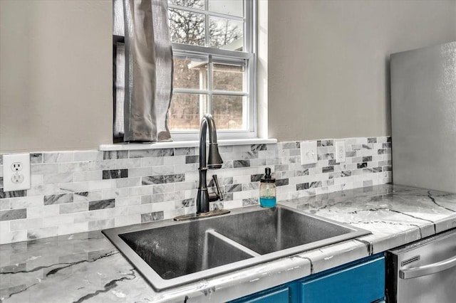 kitchen featuring light stone counters, backsplash, a sink, blue cabinets, and dishwasher