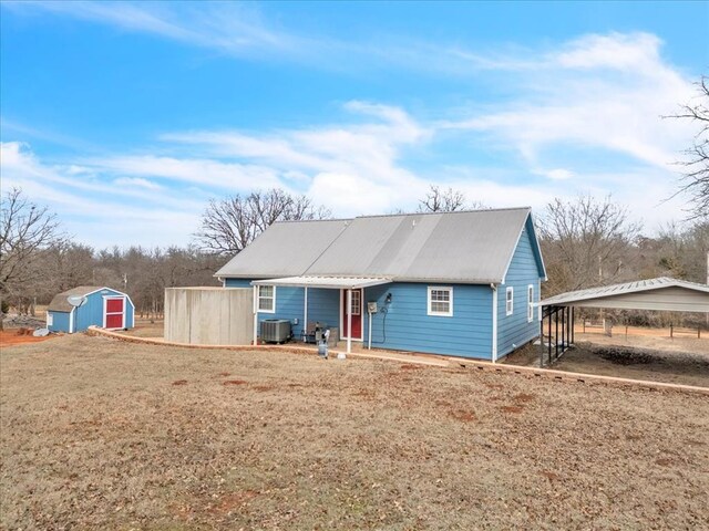 back of house featuring a detached carport, a lawn, central AC unit, a shed, and an outdoor structure