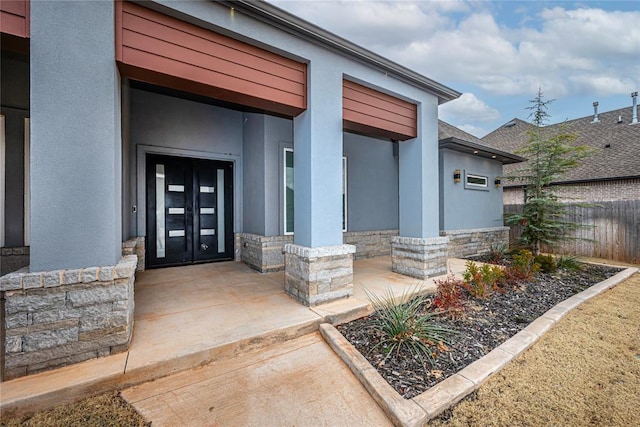 property entrance with stone siding, french doors, and stucco siding