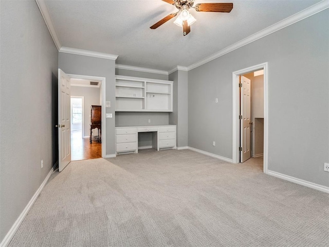 unfurnished living room featuring ornamental molding, baseboards, light colored carpet, ceiling fan, and built in study area