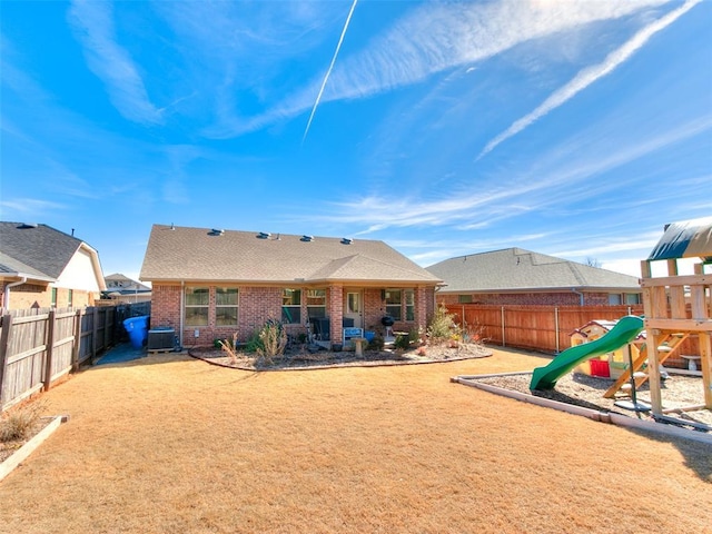 back of property with a fenced backyard, central AC unit, a playground, and brick siding