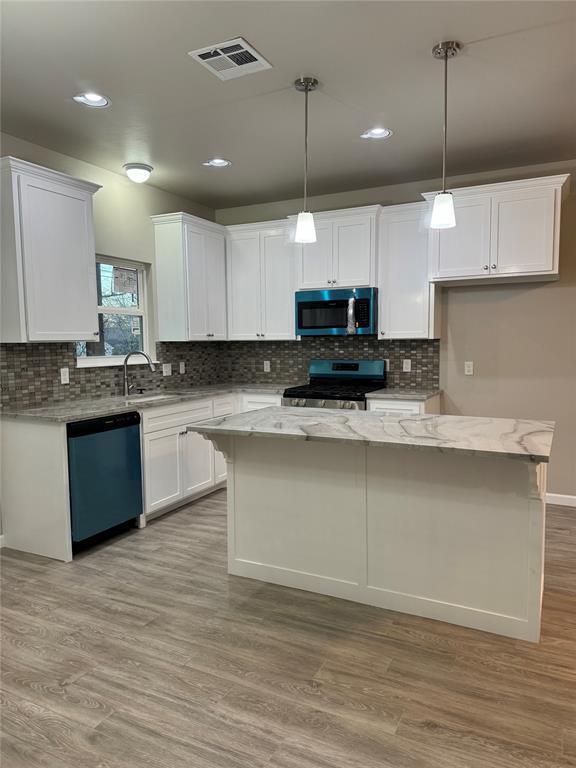 kitchen featuring visible vents, appliances with stainless steel finishes, white cabinets, and decorative light fixtures