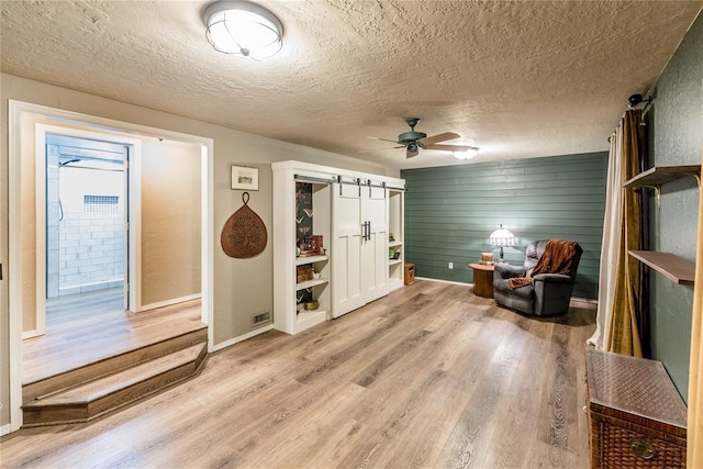 interior space featuring a barn door, baseboards, ceiling fan, a textured ceiling, and light wood-type flooring