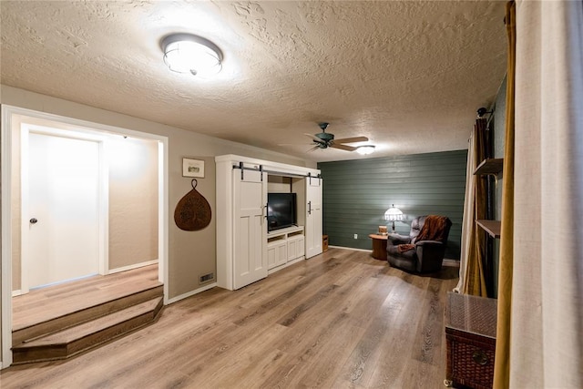 living area with a barn door, ceiling fan, a textured ceiling, wood finished floors, and baseboards