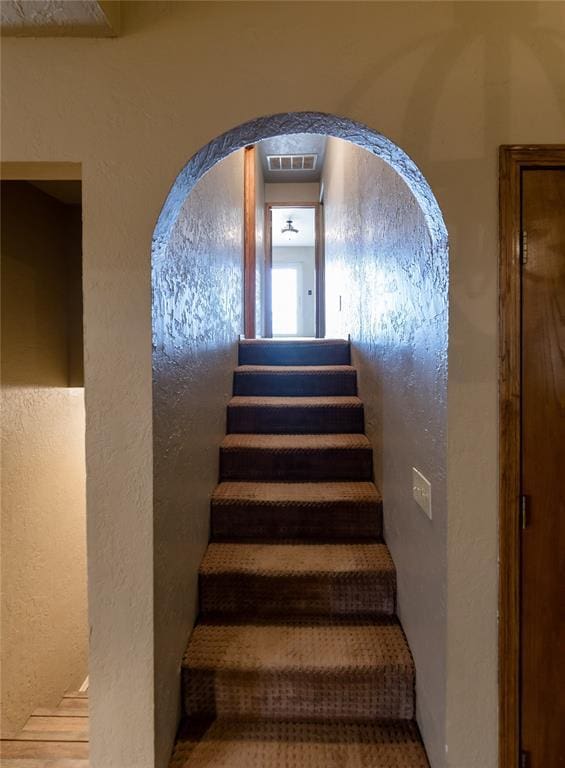 stairway featuring visible vents and a textured wall