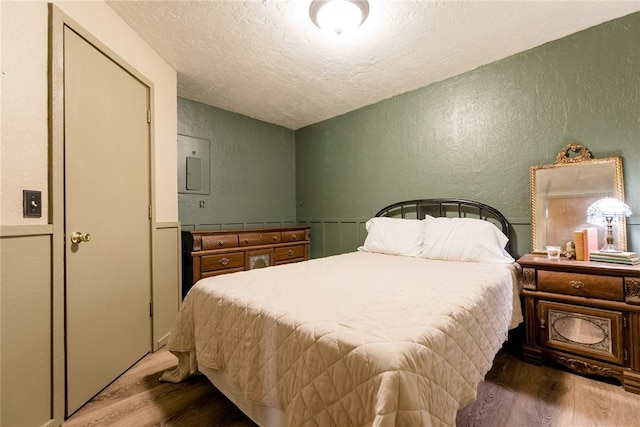 bedroom featuring electric panel, a textured wall, wood finished floors, vaulted ceiling, and a textured ceiling